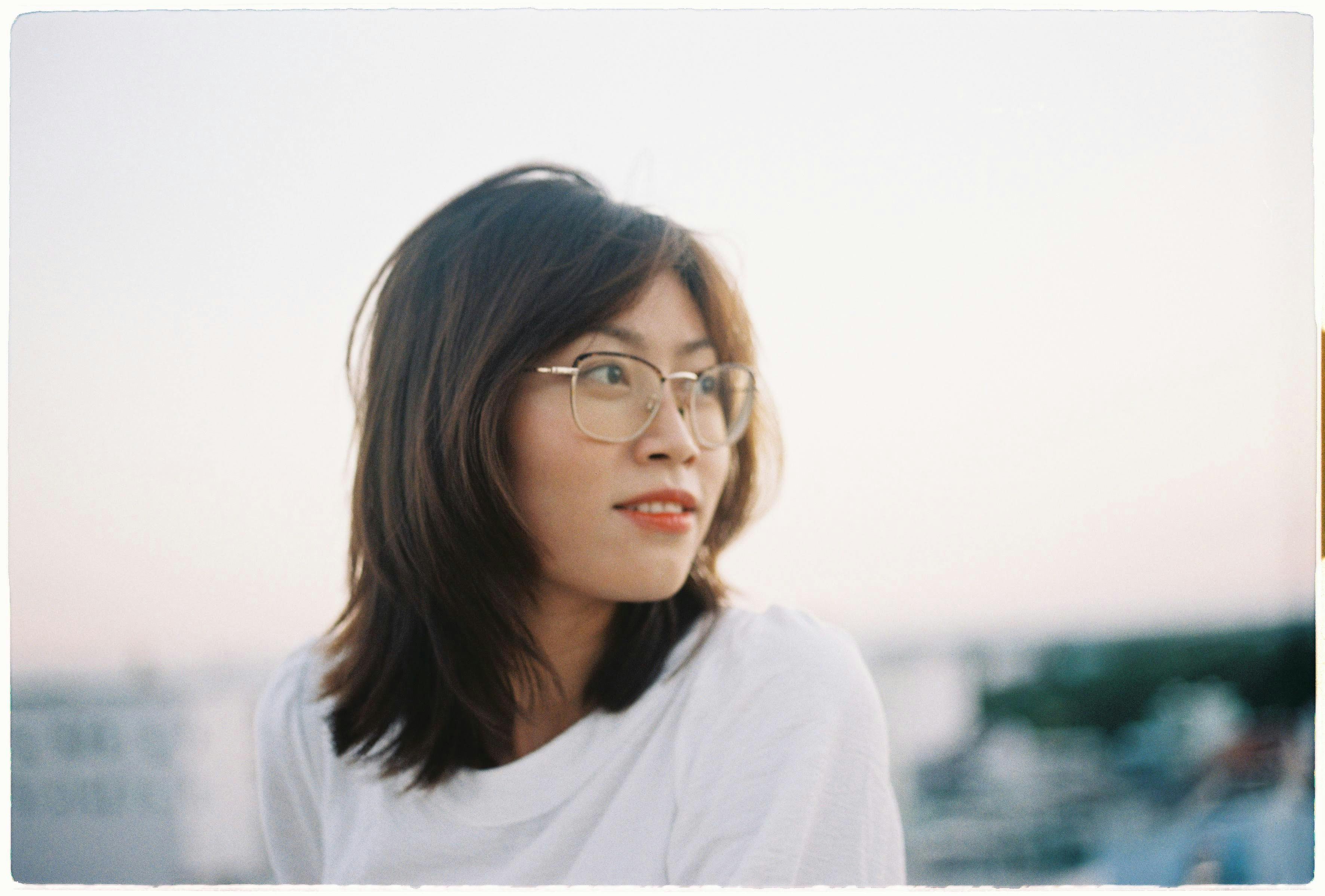 A serene young woman wearing eyeglasses, looking away outdoors during sunset.