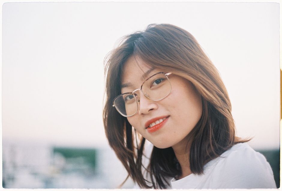 Charming outdoor portrait of a young woman smiling warmly with eyeglasses.
