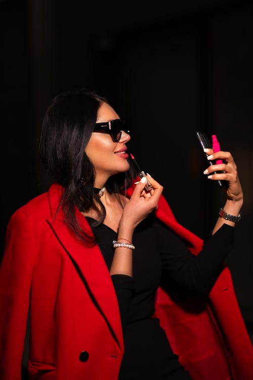 A woman in a red coat and black dress holding a red lipstick