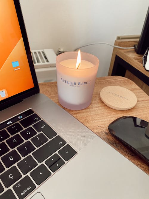A laptop with a candle and a mouse on a desk