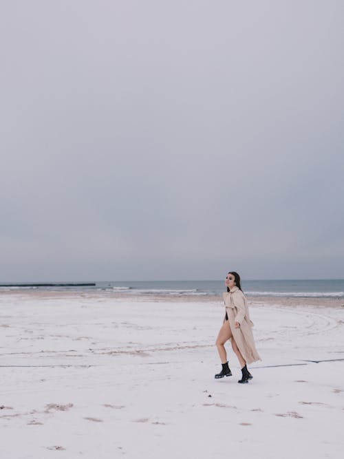 A woman in a trench coat walking on the beach