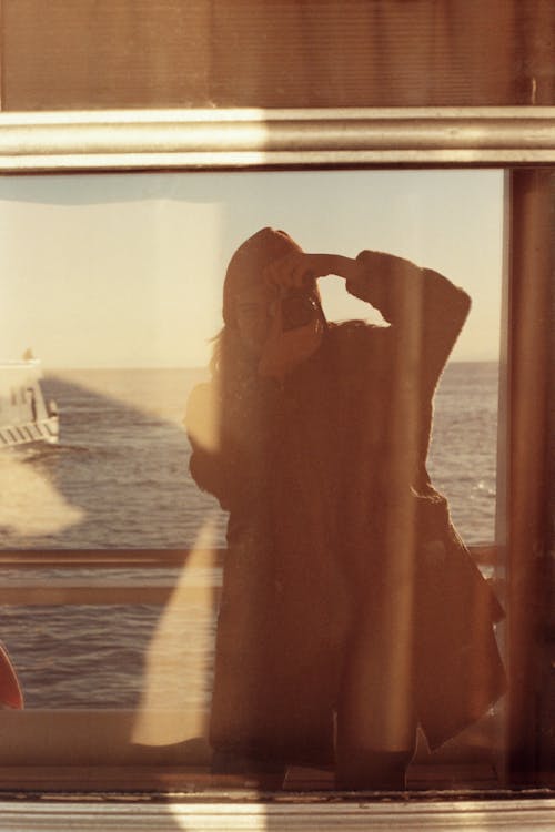 A woman taking a photo of the ocean from a window