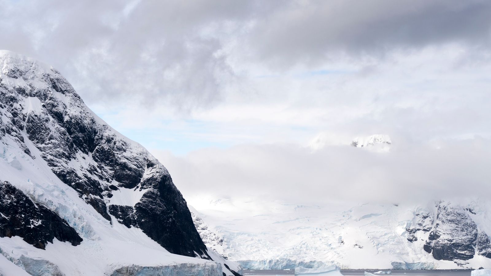 Sheer snow-covered cliffs and drifting ice lining a narrow Antarctic channel.