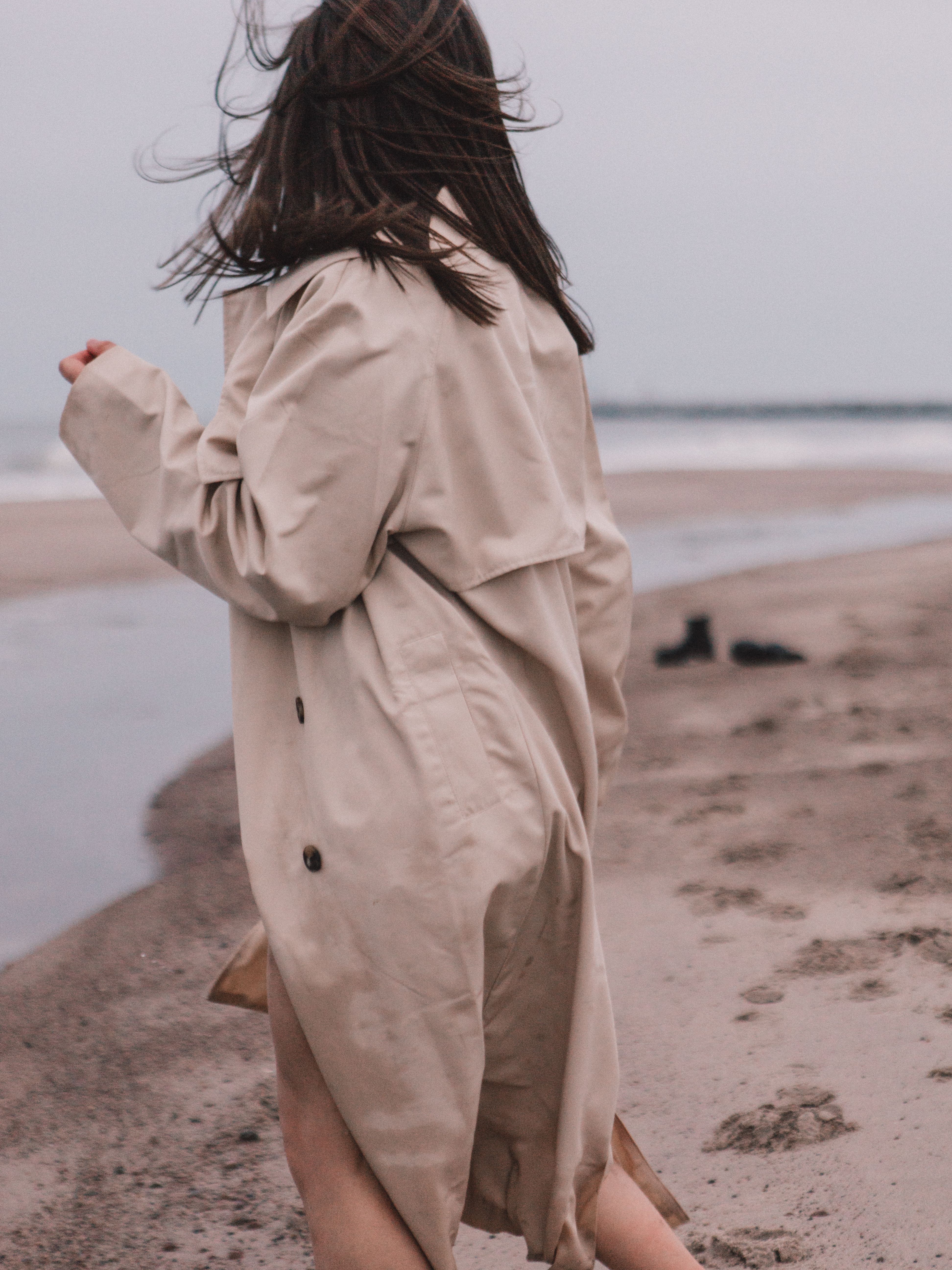 A woman walking on the beach in a trench coat · Free Stock Photo