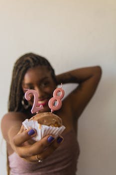 A woman holds a cupcake with '28' candles, celebrating her birthday with joy.