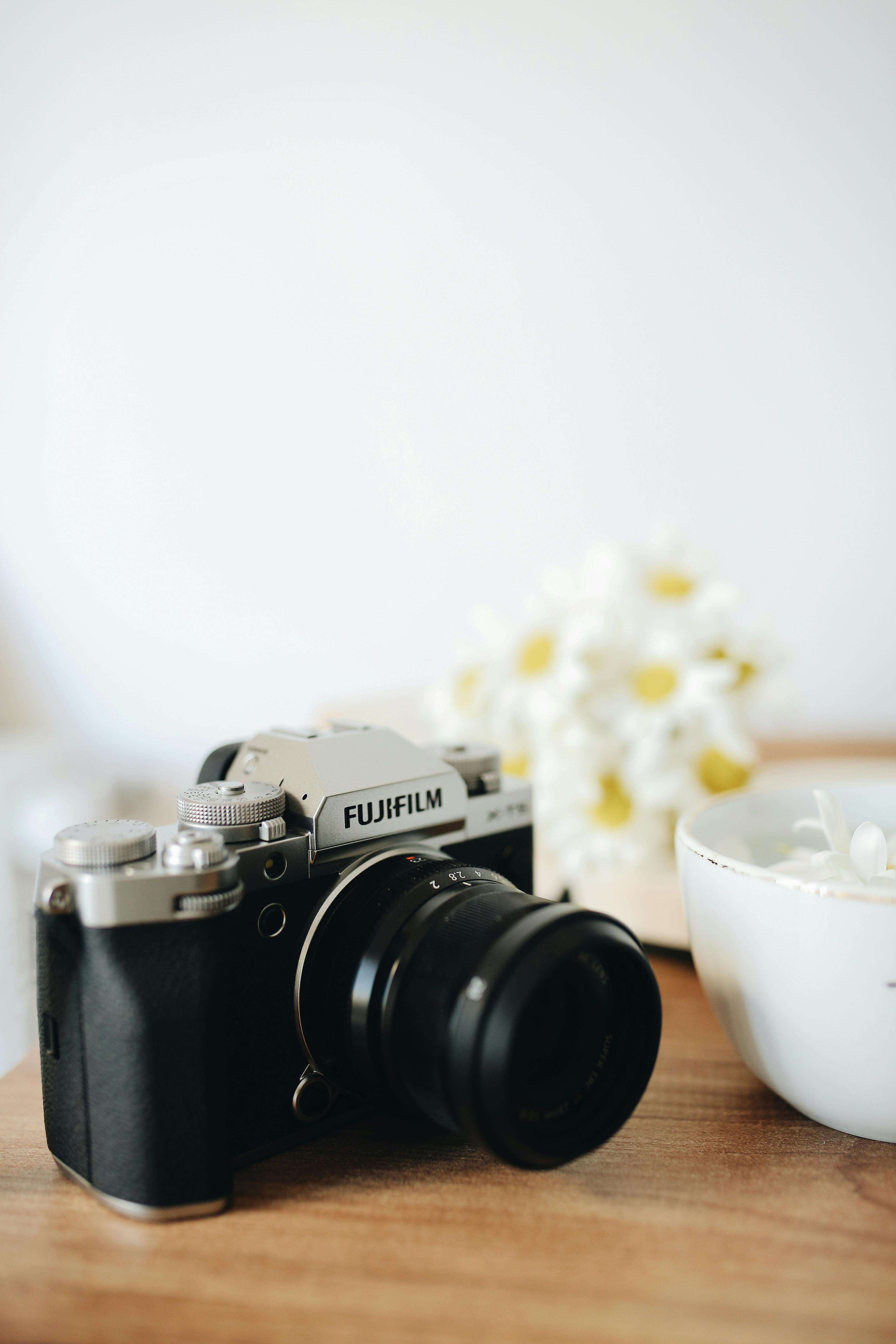 Fujifilm camera next to a cup and flowers on a wooden table.