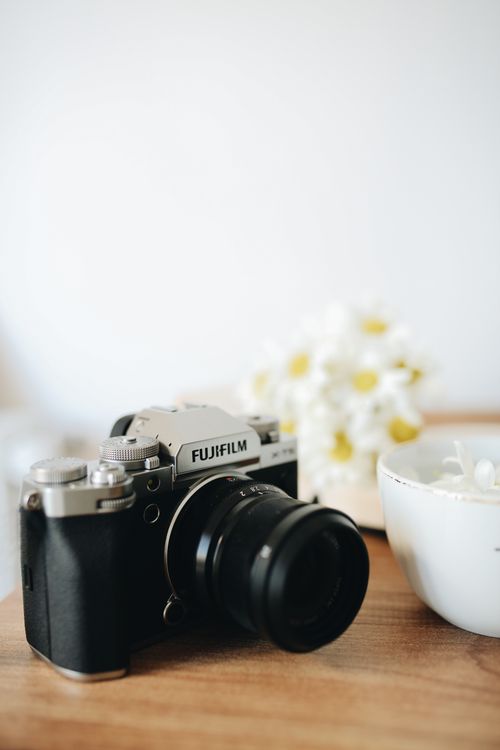 Free Fujifilm camera next to a cup and flowers on a wooden table. Stock Photo