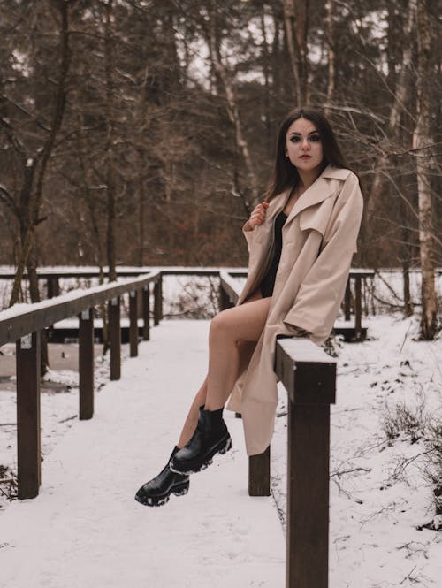 A woman in boots and a coat sitting on a wooden rail