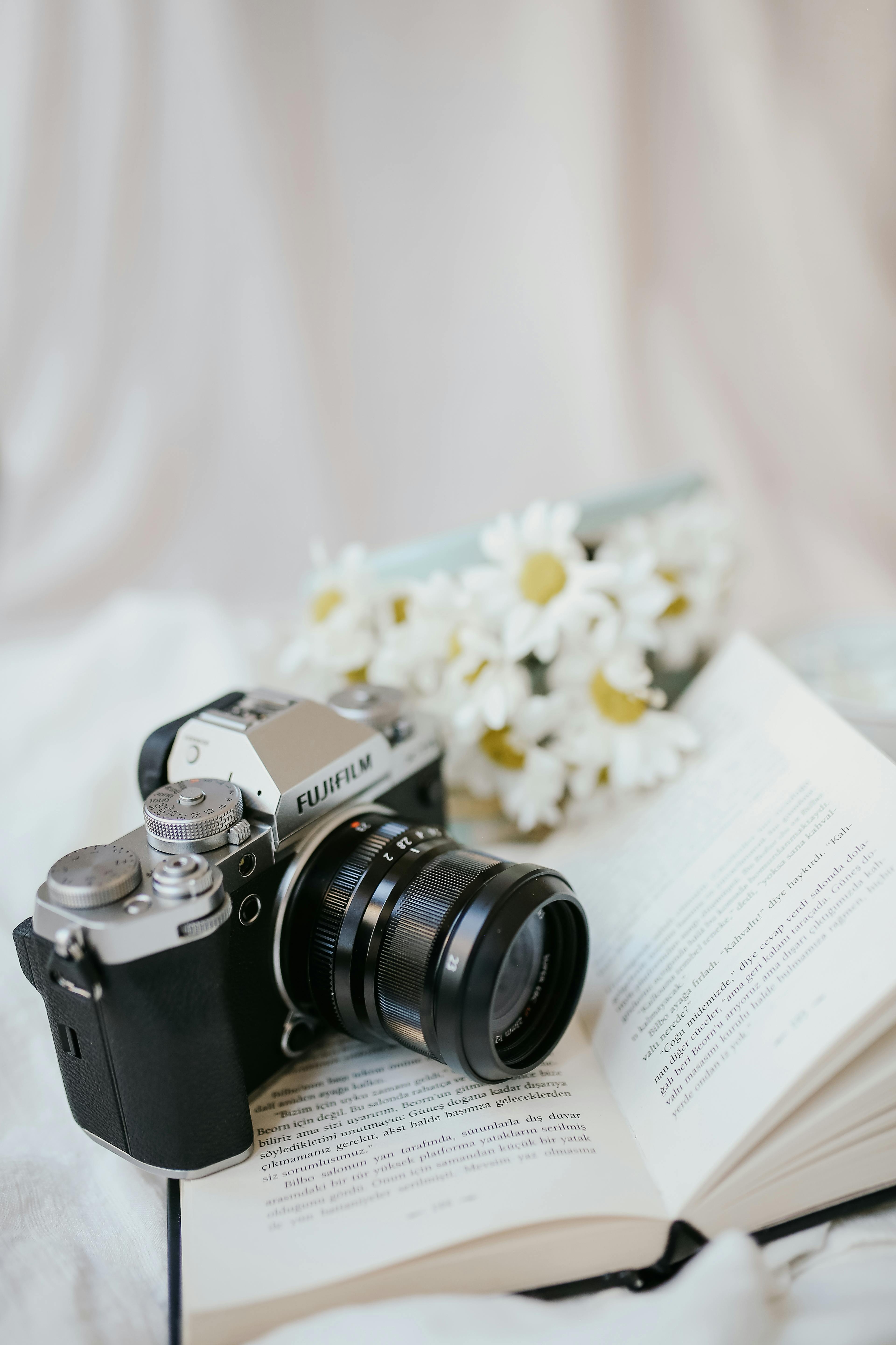 A classic film camera on an open book with daisies in the background, providing nostalgic vibes.