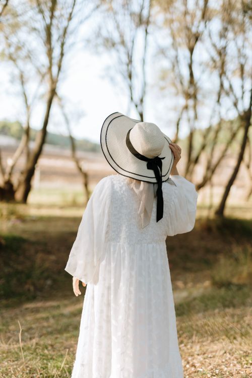 Free A woman in a white dress and hat enjoys a sunny day in a tranquil park. Stock Photo