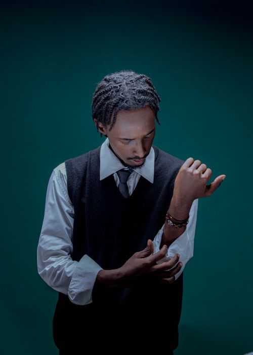Free Stylish man with braided hair in a shirt and sweater vest adjusting his sleeves in a studio setting. Stock Photo