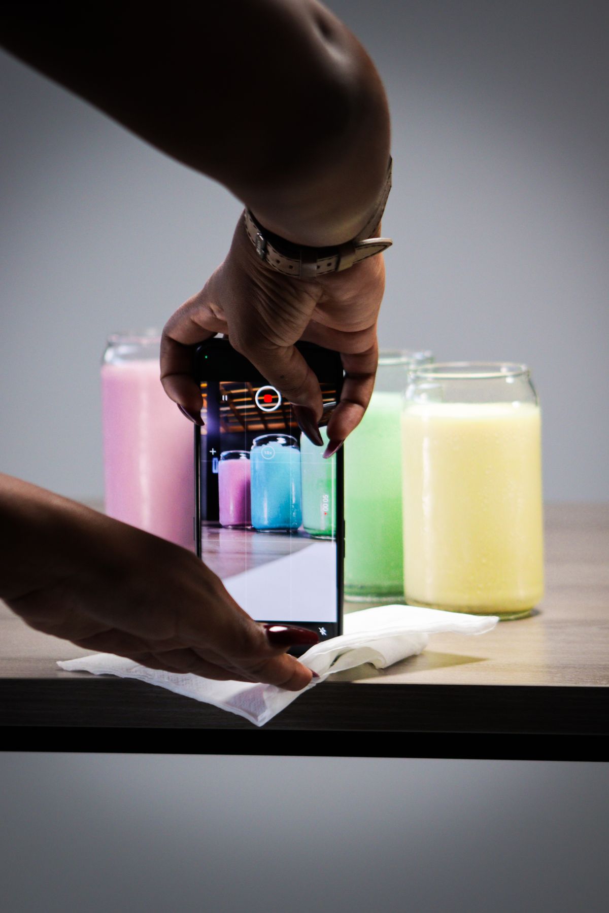 Hands filming colorful product jars with a smartphone