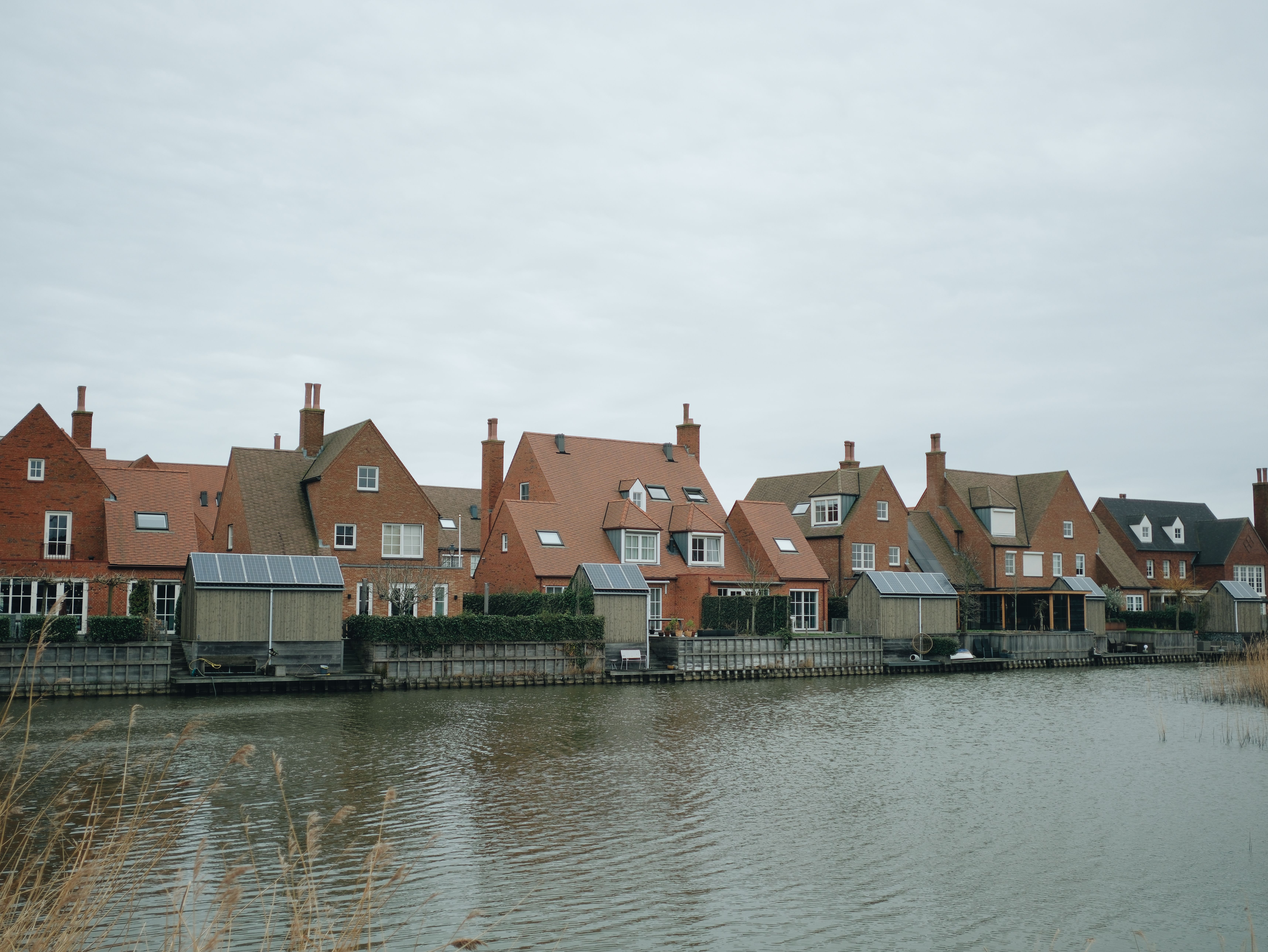 Picturesque row of red brick houses along a tranquil canal under an overcast sky.