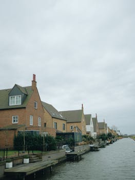 Scenic view of row houses along a tranquil riverbank under cloudy skies, embodying peaceful riverside living.