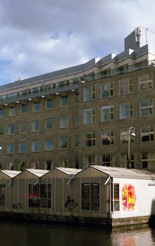 在多云的天空下，阿姆斯特丹运河旁的现代建筑展示着城市风貌