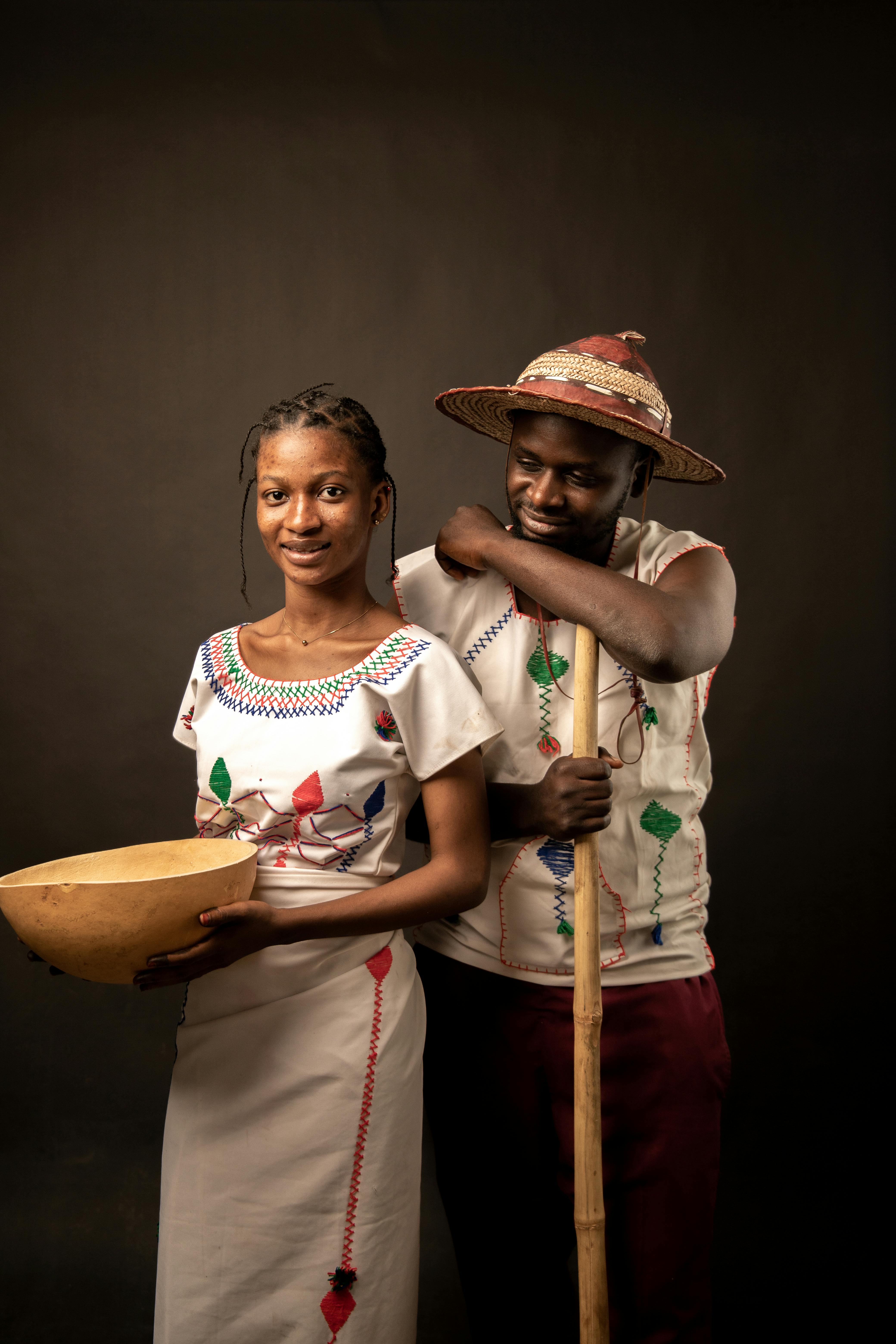 Portrait of a Nigerian man and woman in traditional attire holding a wooden bowl, captured in a studio setting.