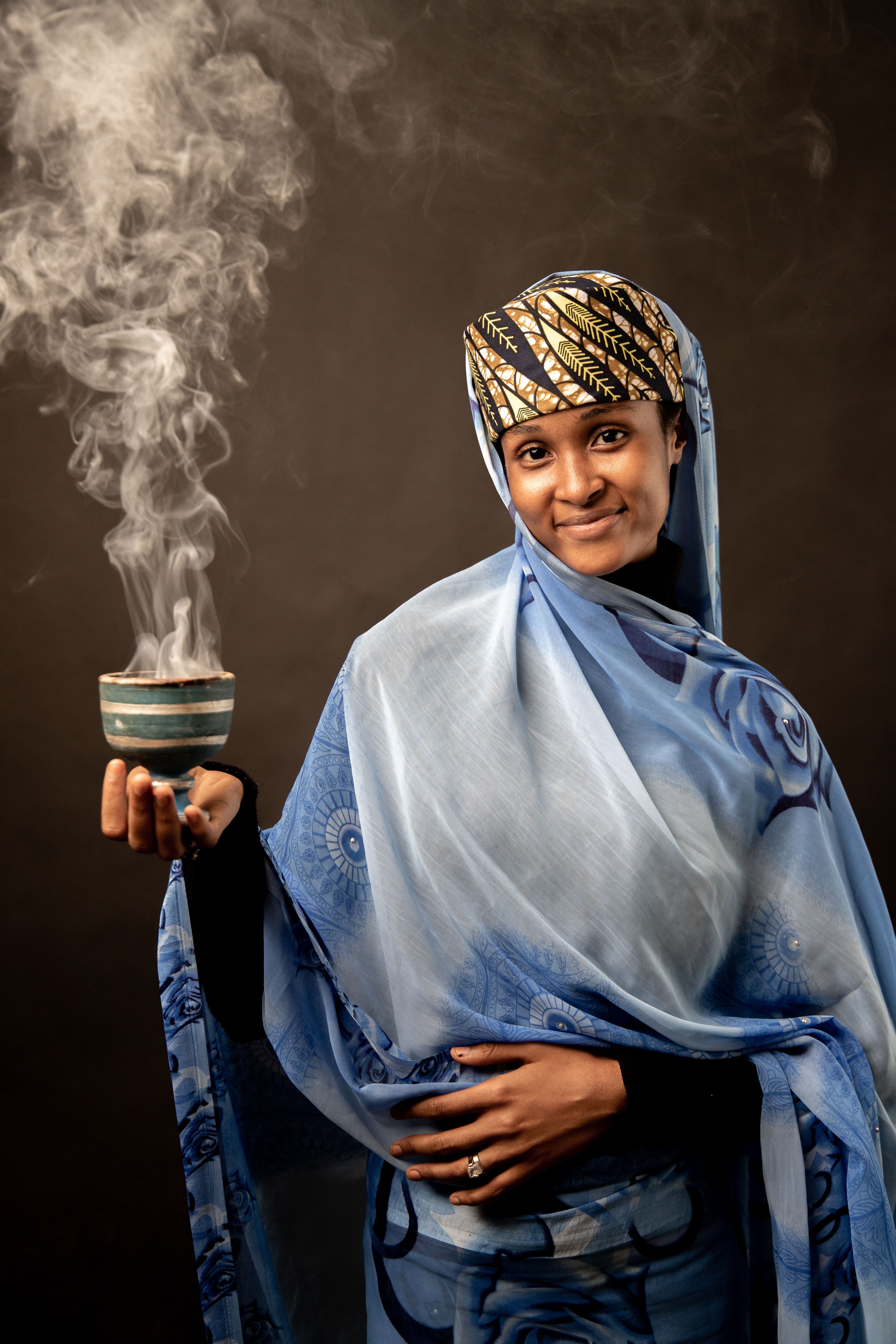 A woman in a blue and white scarf holding a cup of smoke · Free Stock Photo