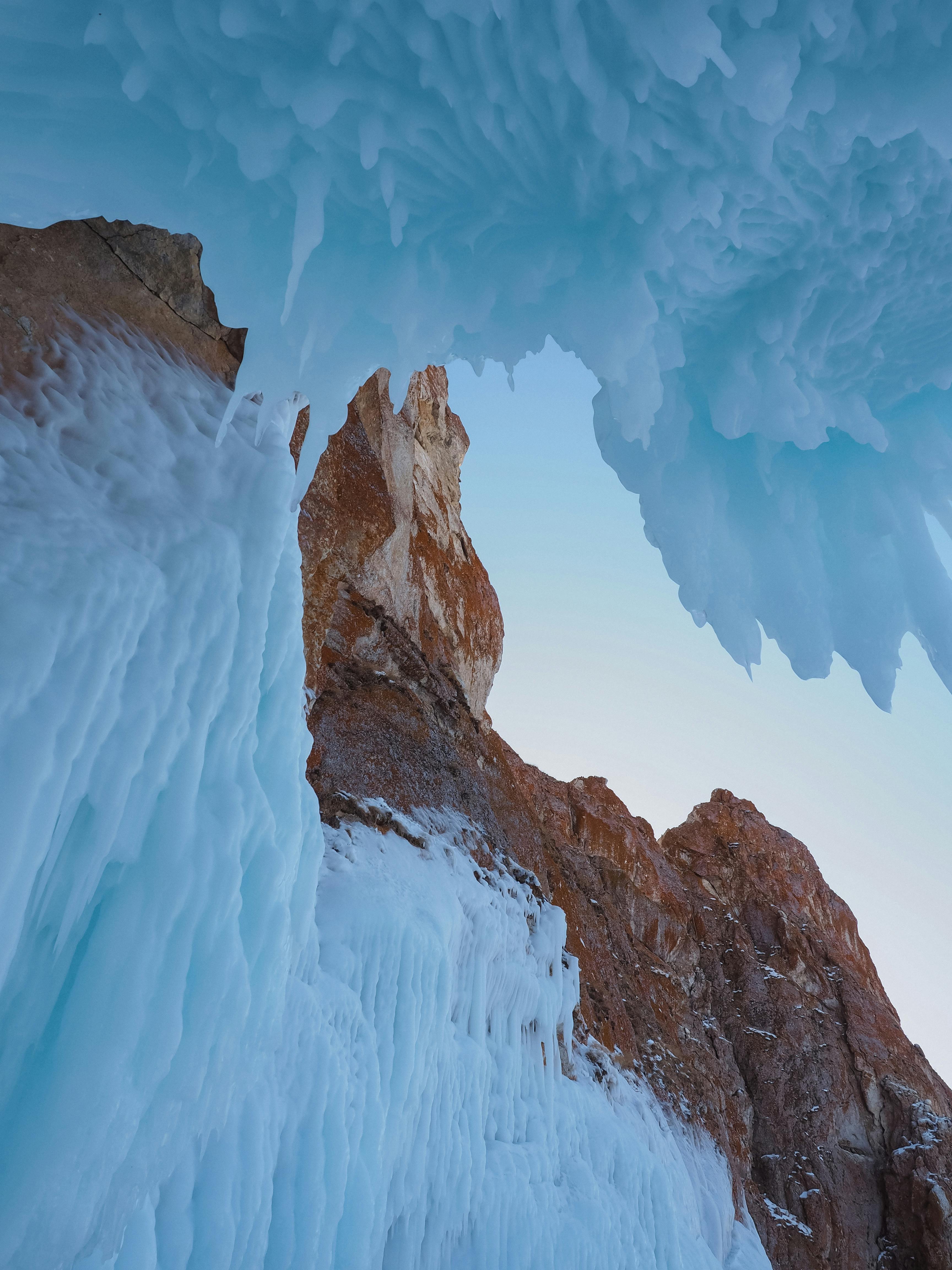 Ice formations cascade from red rocks at Lake Baikal, creating a stunning winter spectacle.