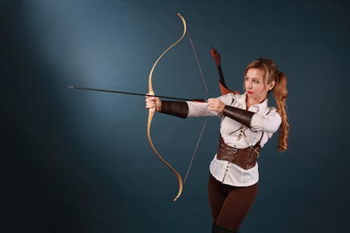 A woman in a brown shirt and brown pants is holding a bow