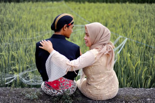 Free Romantic couple wearing traditional clothes sitting together by a paddy field. Stock Photo