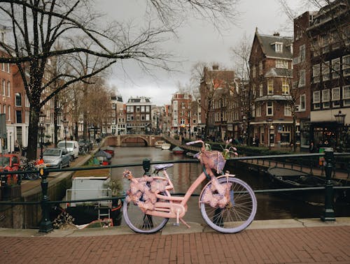 A pink bicycle parked on a bridge over a canal