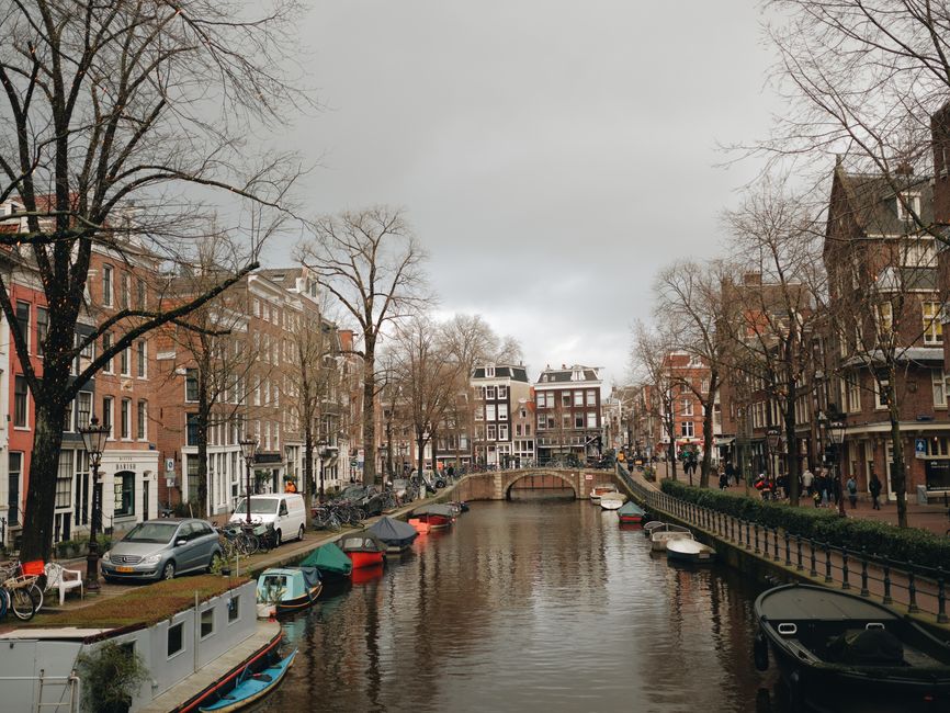 Scenic view of Amsterdam canal with boats, townhouses, and a bridge. Perfect urban travel destination.