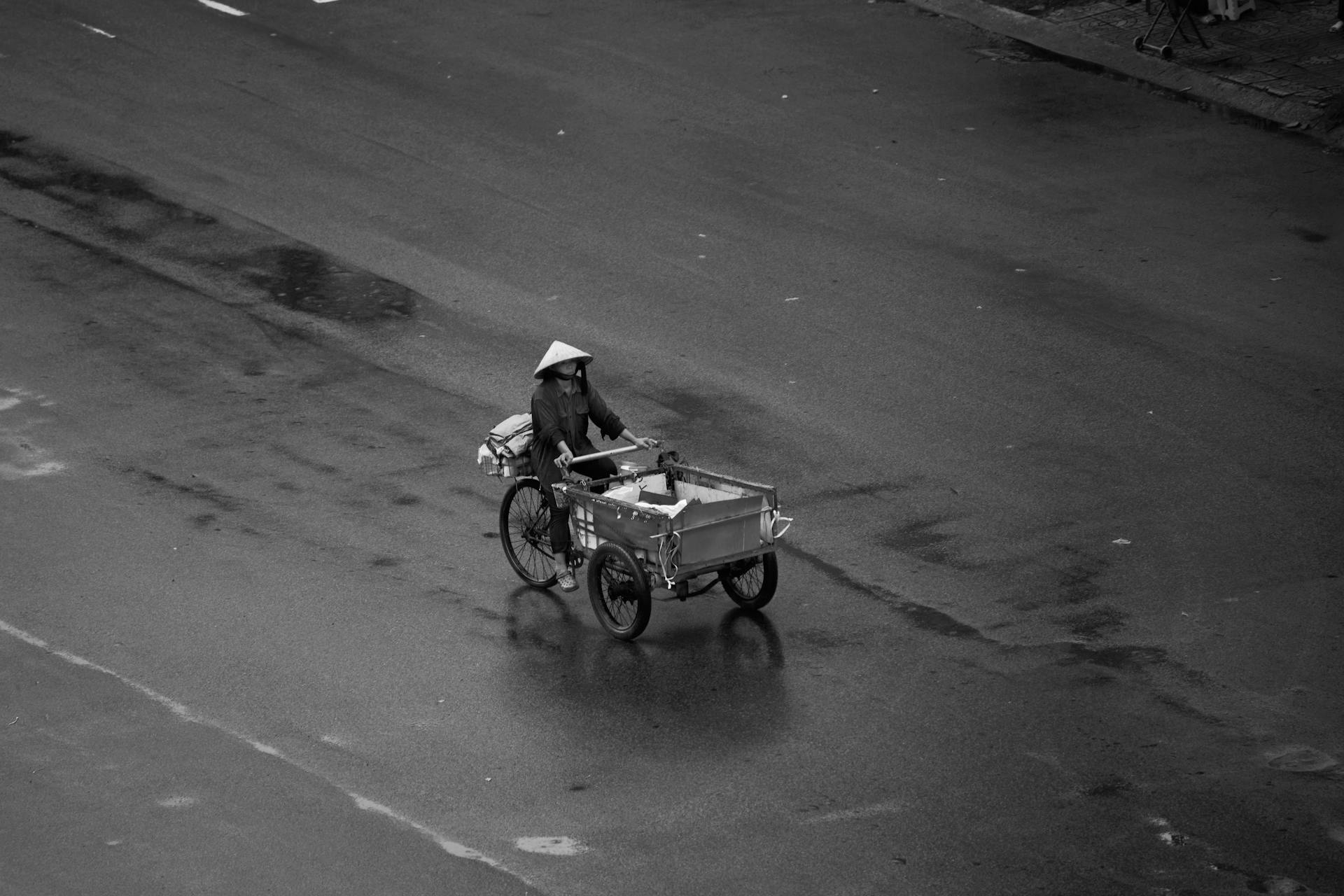 Black and white image of a person riding a cargo bicycle on an empty city street.