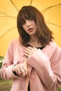 一位撑着黄色雨伞、身穿粉色外套的年轻女子正在户外享受时尚时刻