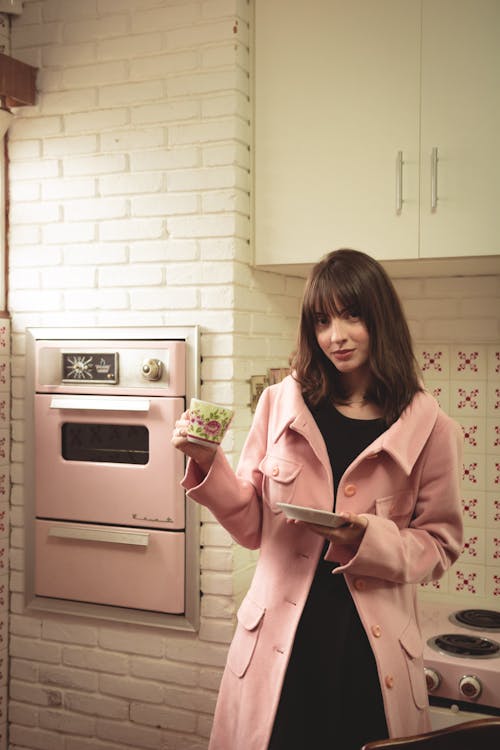 Woman Wearing Pink Coat Holds Cup and Saucer at the Kitchen Area