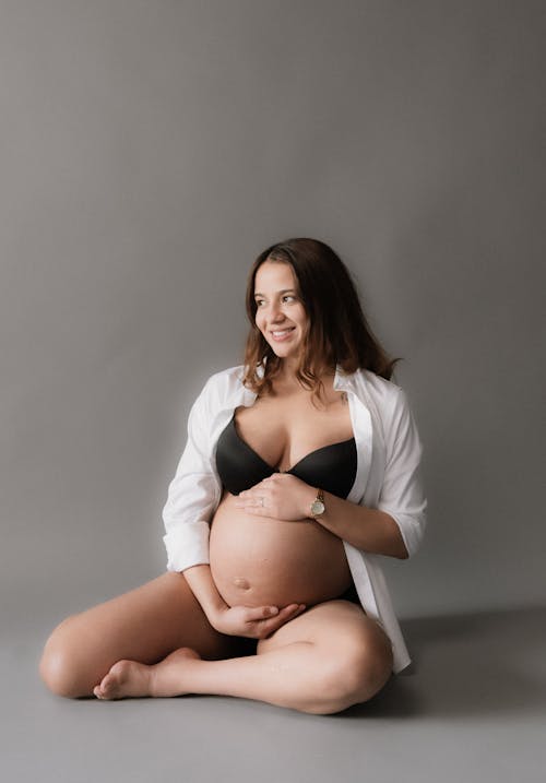 A pregnant woman in a white shirt and black underwear
