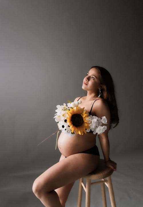 A pregnant woman in a flowery bikini sits on a stool