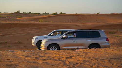 Two suvs are parked in the desert with sand dunes in the background