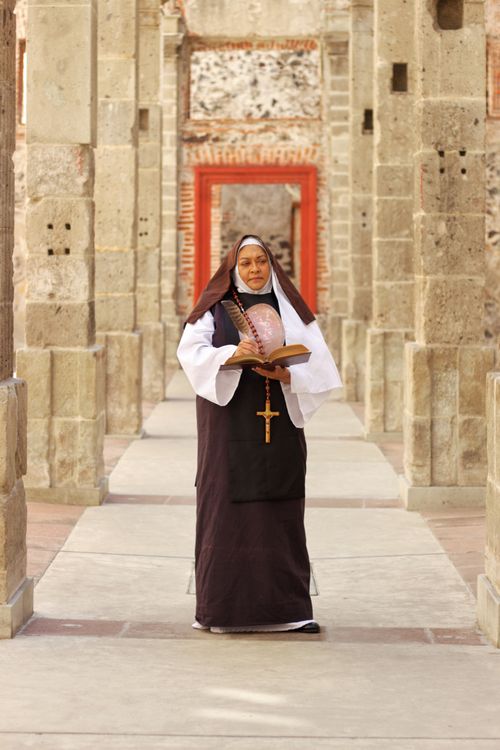 Free A nun stands in a stone hallway, reading a religious book with contemplation. Stock Photo