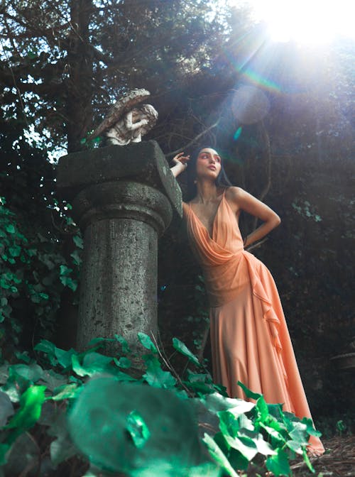 A woman in an orange dress posing near a statue