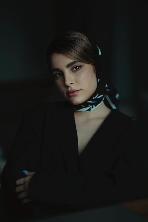 Free A portrait of a woman in a black blazer and scarf, exuding elegance in a dimly lit setting. Stock Photo