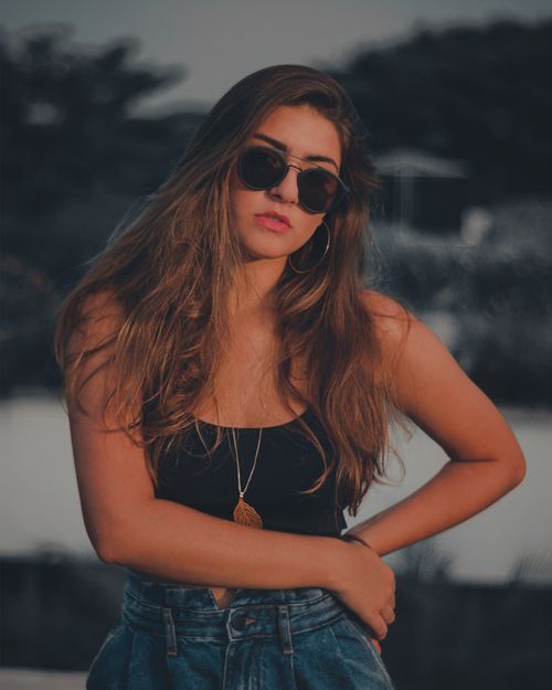 Free Stylish woman wearing sunglasses and casual attire posing outdoors in an evening setting. Stock Photo