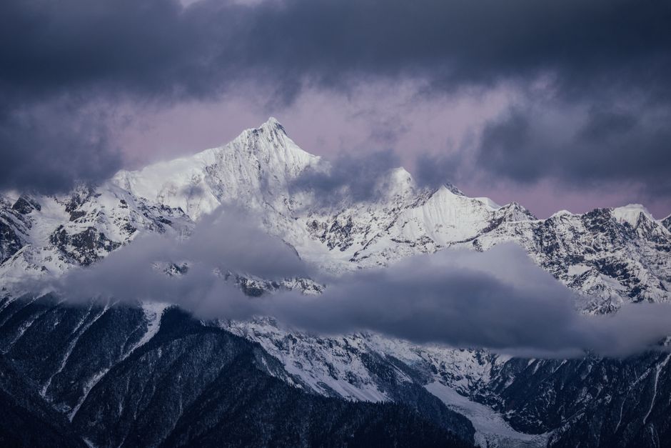 A breathtaking view of snow-covered peaks under a moody twilight sky, surrounded by clouds.