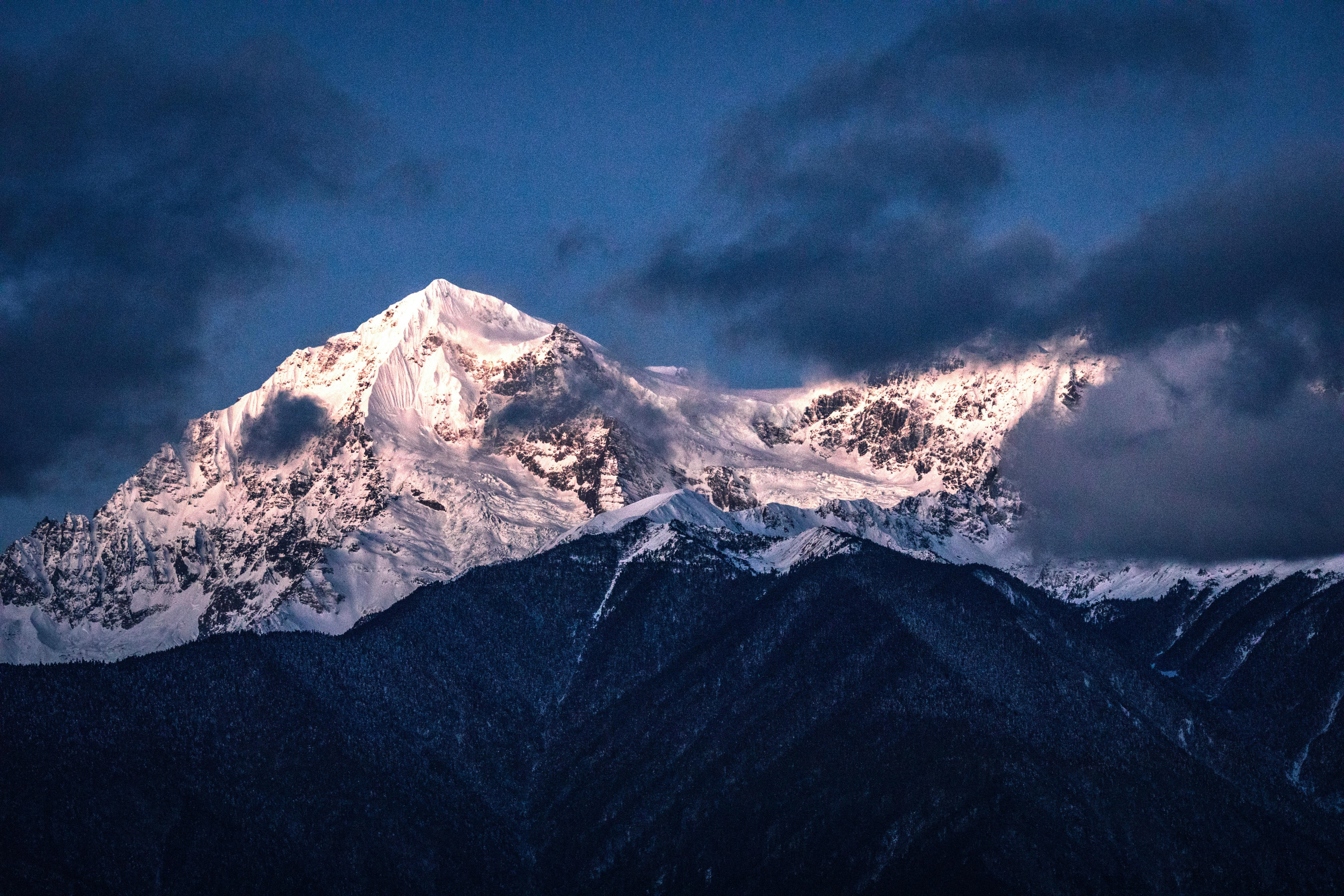Stunning mountain landscape with snow-capped peaks illuminated at twilight, surrounded by clouds.