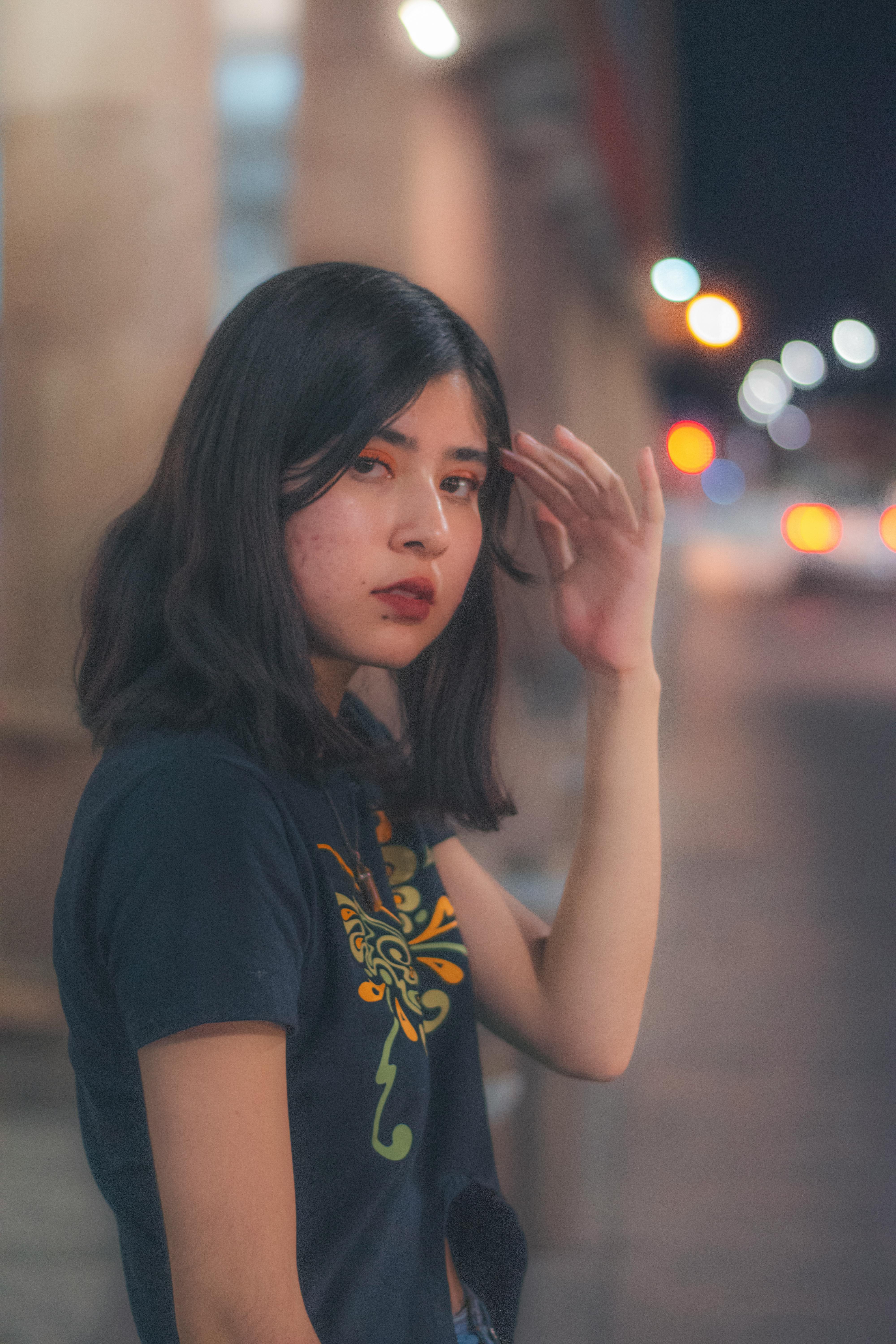 Portrait of a young woman posing in a city street at night, with blurred lights in the background.