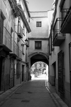 Black and white view of a narrow street with arches in Lorca, Spain.
