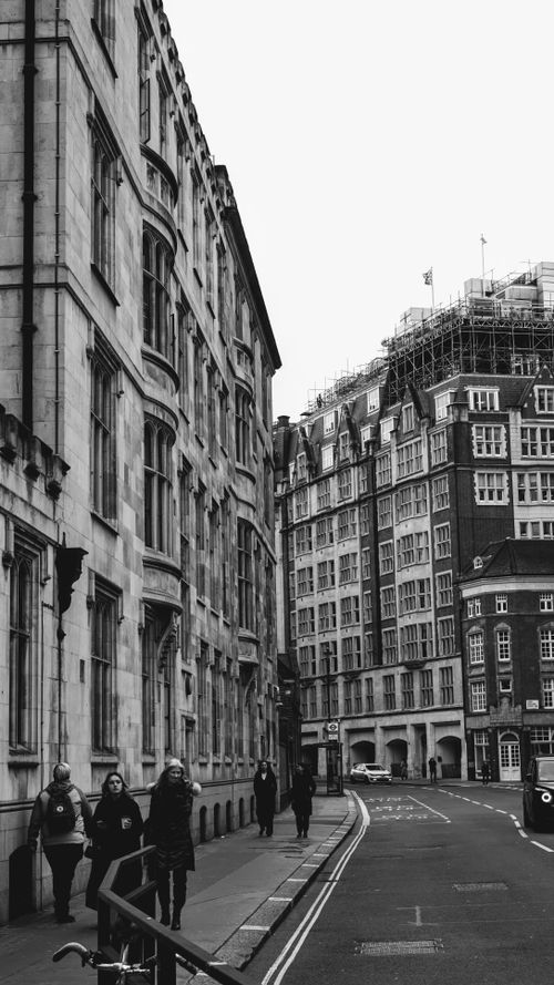 Free Black and white photo of pedestrians walking along historic city street with classic architecture. Stock Photo