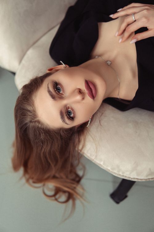 Free A young woman with brown hair elegantly poses on a sofa indoors, showcasing serene beauty. Stock Photo