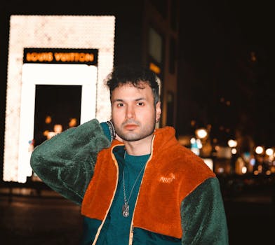 Man posing stylishly at night in Frankfurt, showcasing urban fashion against a city backdrop.