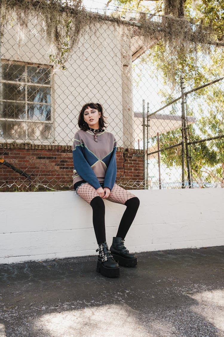 Woman In Sweatshirt And Over Knee Stocking Sits On Wall