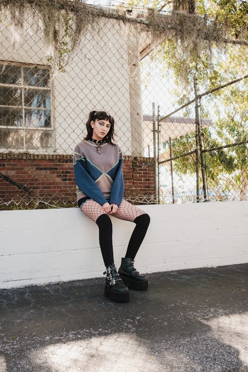 Woman in Sweatshirt and Fishnet Stocking Sits on Wall