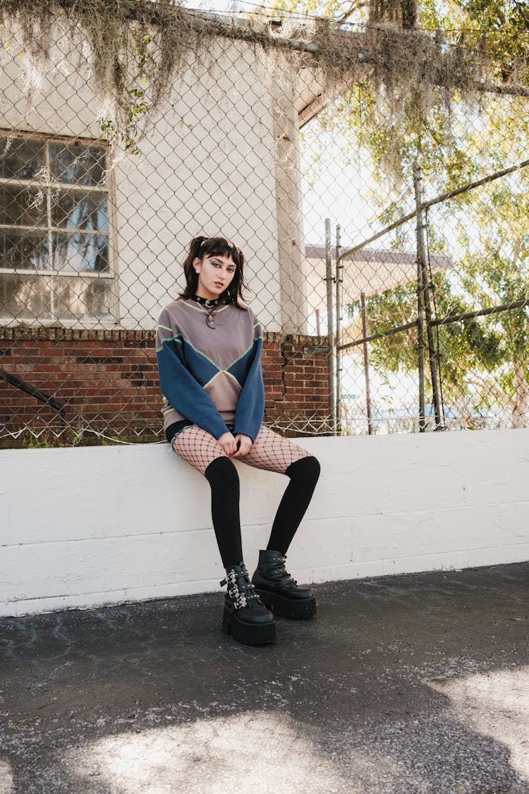 Woman In Sweatshirt And Fishnet Stocking Sits On Wall