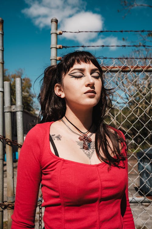 A woman with tattoos and piercings standing in front of a fence