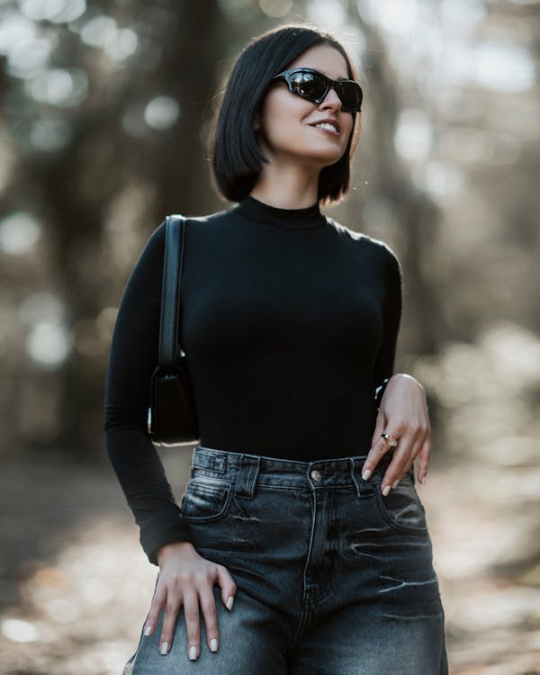 A woman in black top and jeans standing in the woods