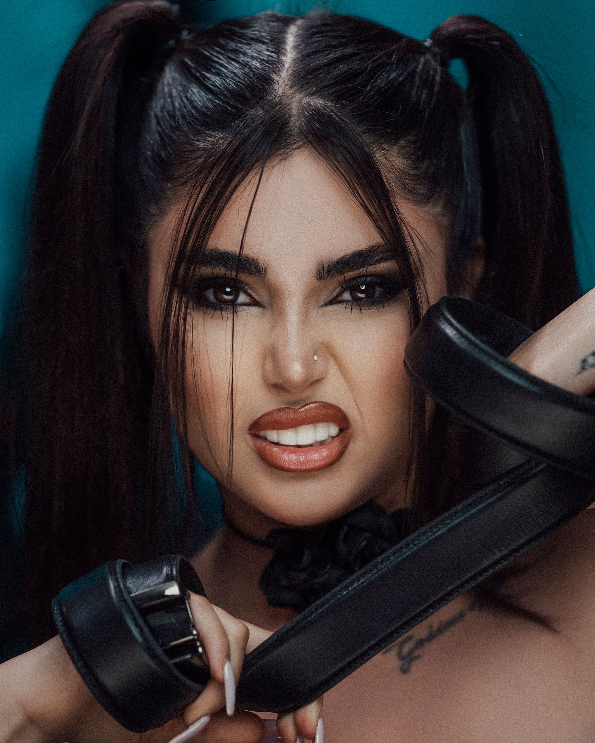 Dramatic close-up portrait of a woman holding a belt with expressive facial expression.
