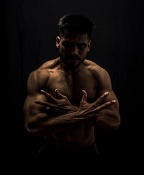 Strong and muscular man posing topless with crossed arms in a studio setting.